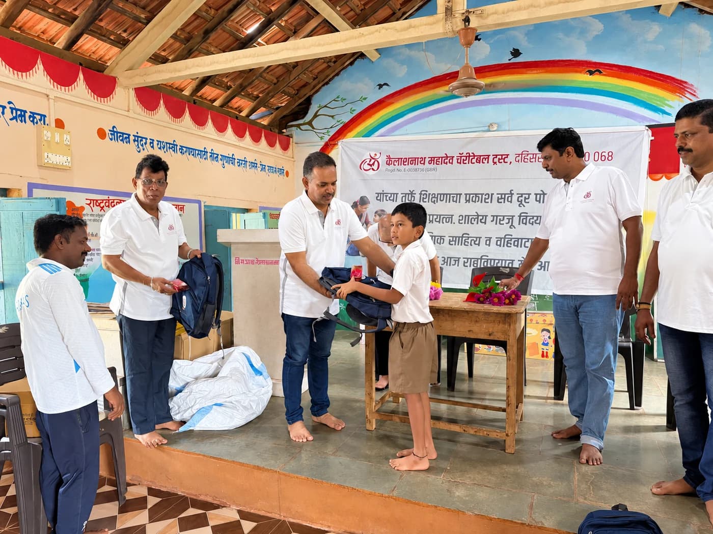 A schoolboy receiving a navy school bag from Trust members in the original rainbow-painted classroom