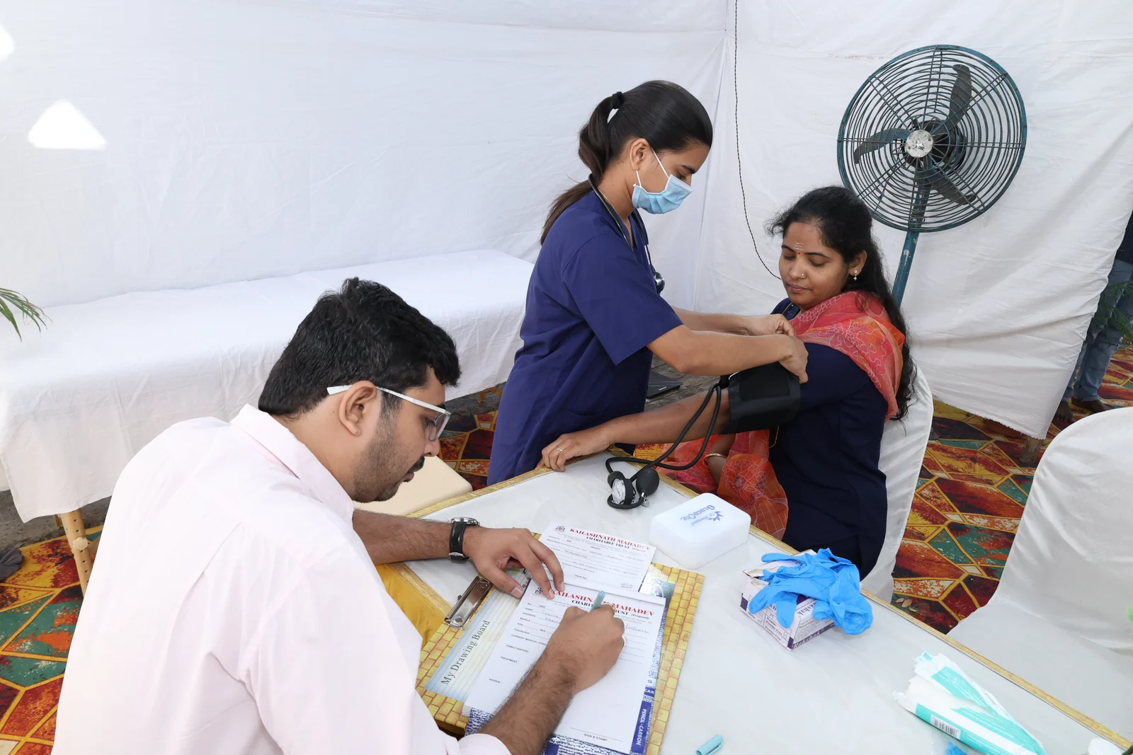 A nurse fitting a blood pressure cuff on a woman's arm while a doctor takes notes