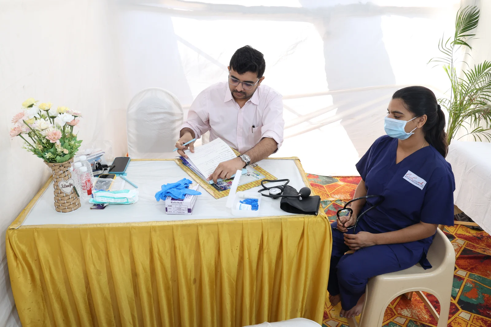 A doctor and nurse at their medical camp station with a blood pressure monitor on the table