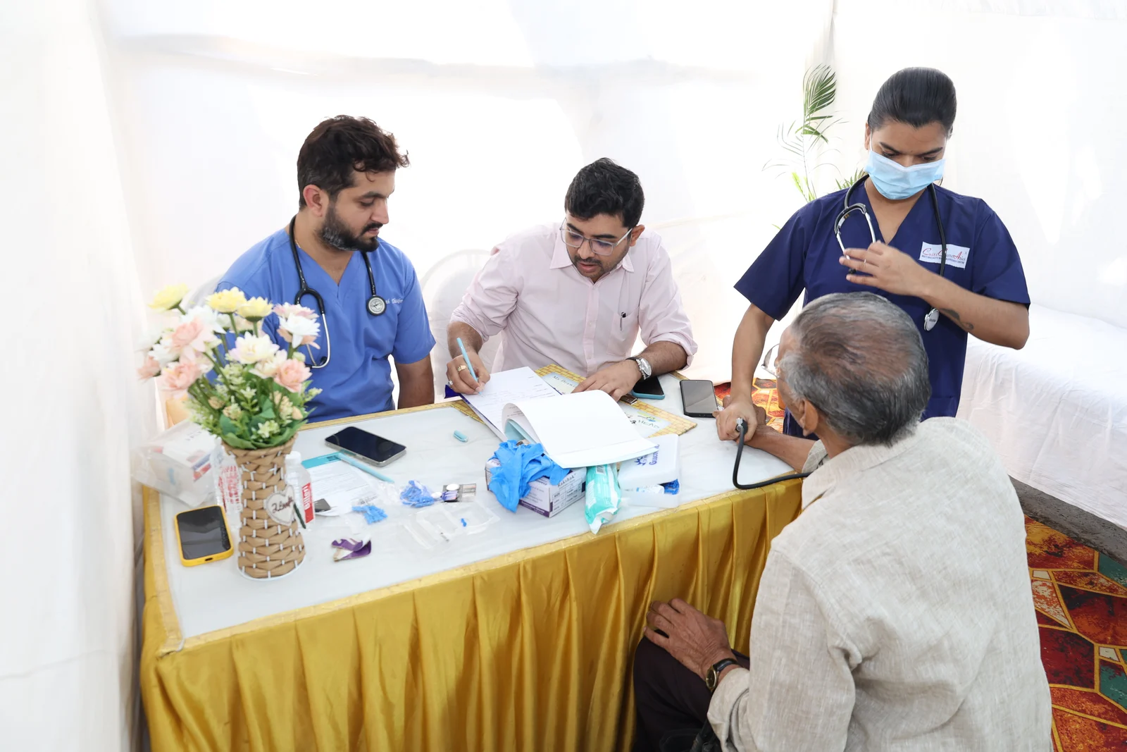 Two doctors and a nurse listening to an older man at the March 2024 medical camp