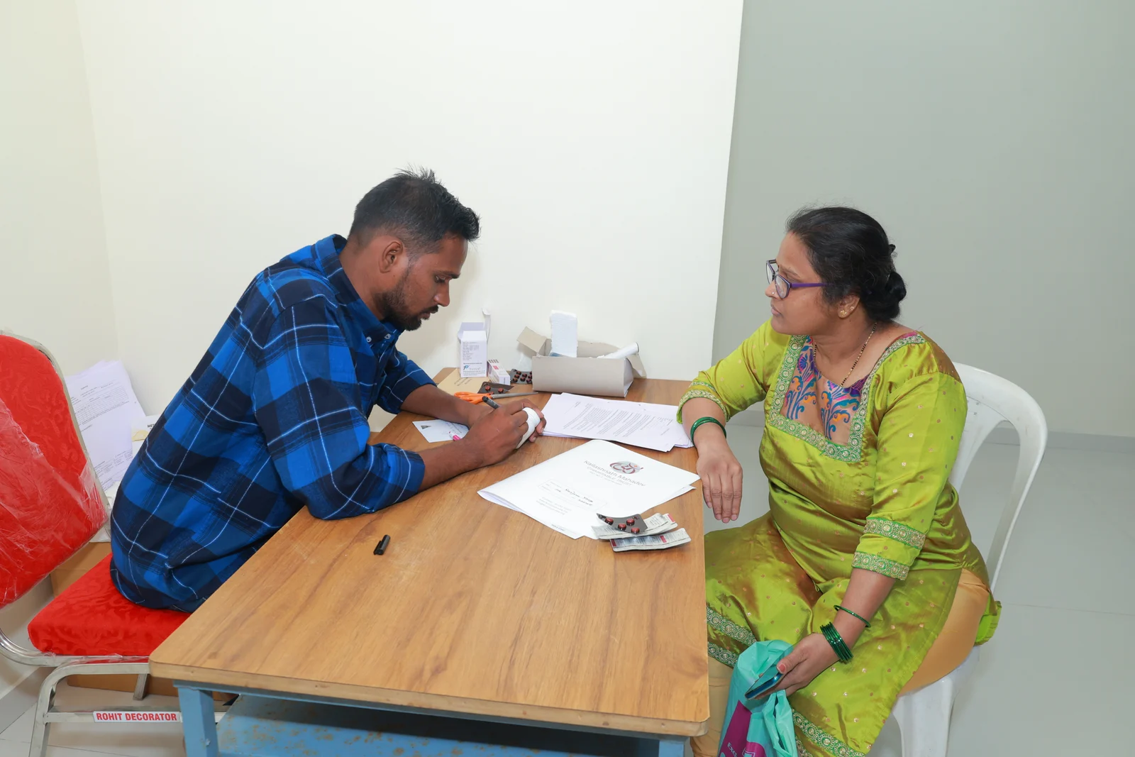 A woman in a green sari speaking with a medical camp team member at his desk