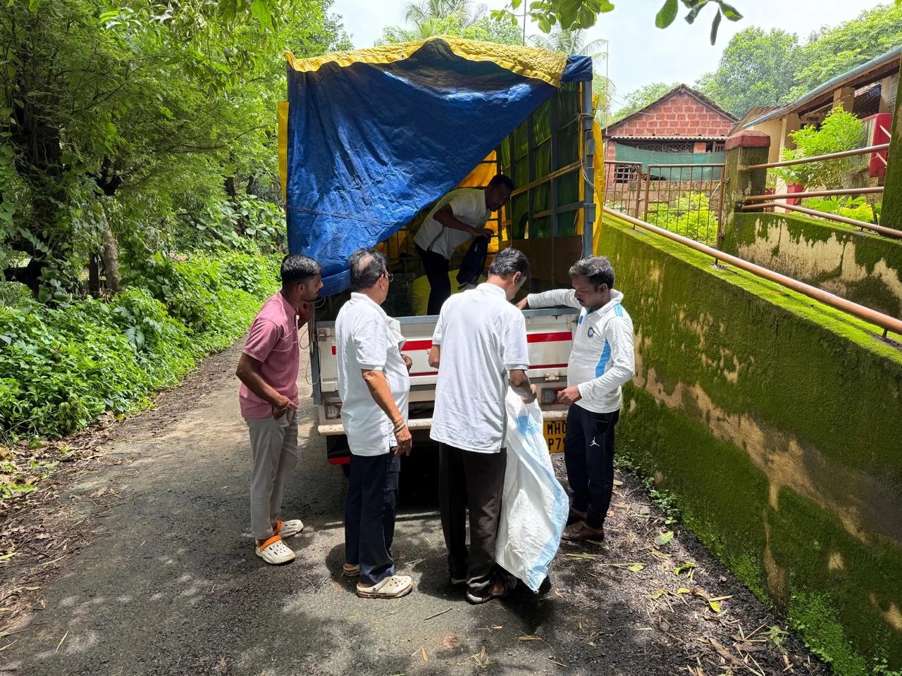 Trust members unloading sacks of supplies from a vehicle beside a green village road