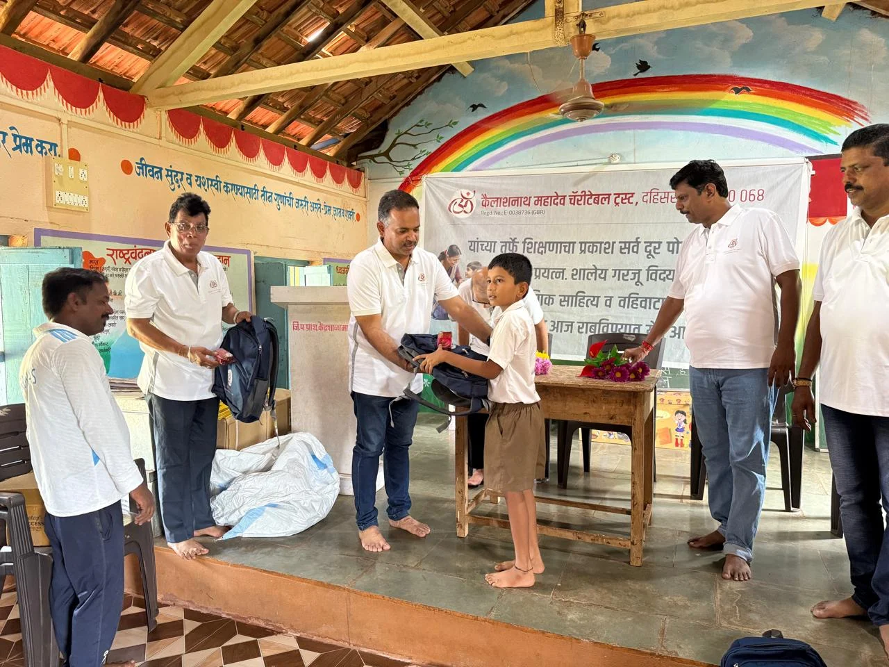 A schoolboy receiving a navy bag from Trust members in a classroom painted with a rainbow