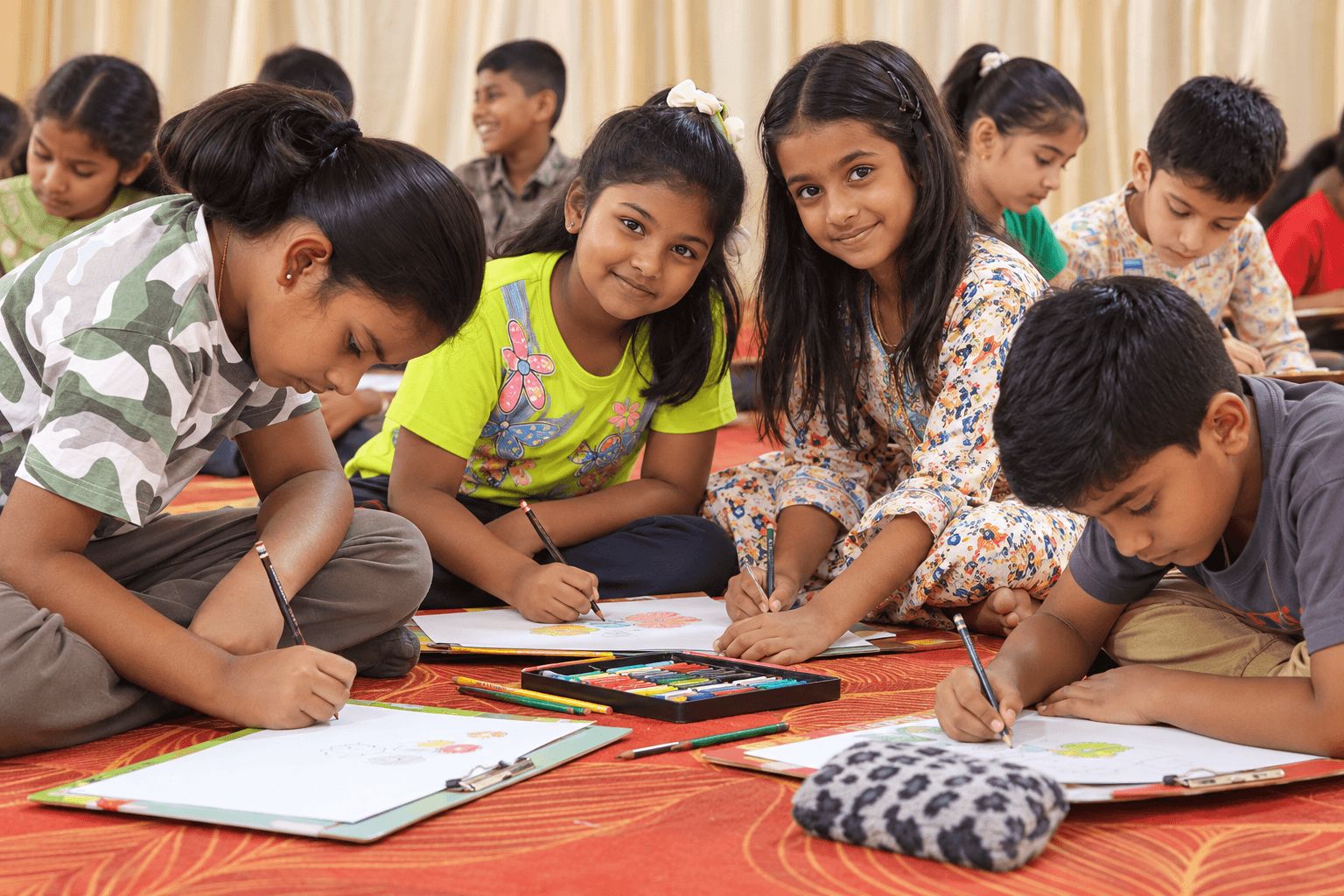 Children drawing with pencils and crayons, sitting together on a red mat